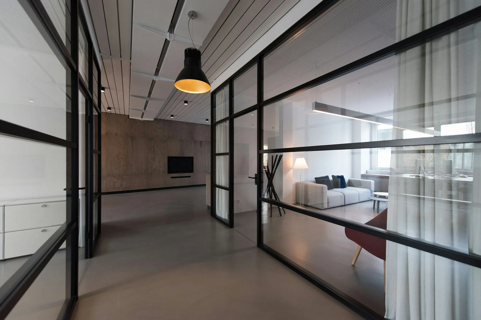 Glass-partitioned office with black steel frames and pendant light